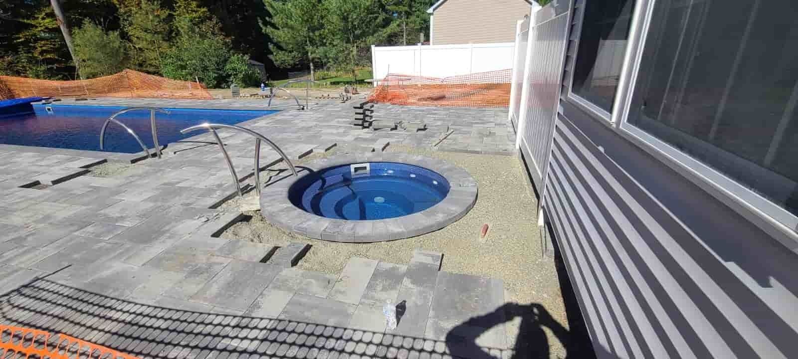Backyard patio with a round in-ground hot tub, pool, and house exterior in sunlight