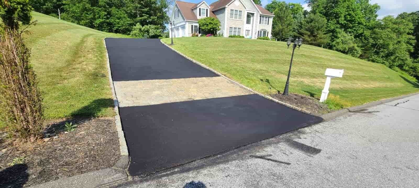 Freshly paved black driveway leading to a house on a green hillside