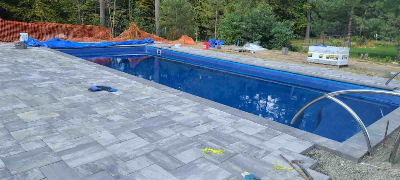 Empty blue in-ground pool under construction beside a gray shingled roof