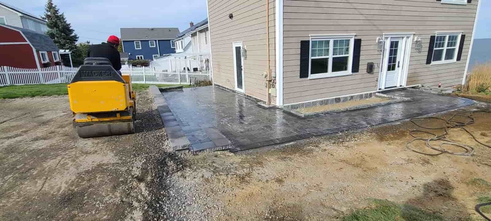Yellow skid steer smoothing wet concrete beside a beige house under construction