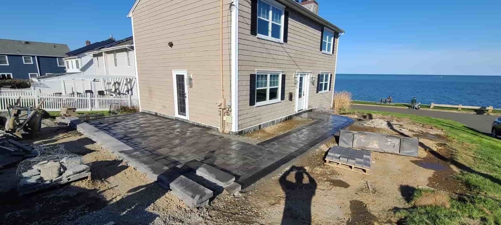 Coastal stone house with paved patio and benches overlooking the ocean on a sunny day