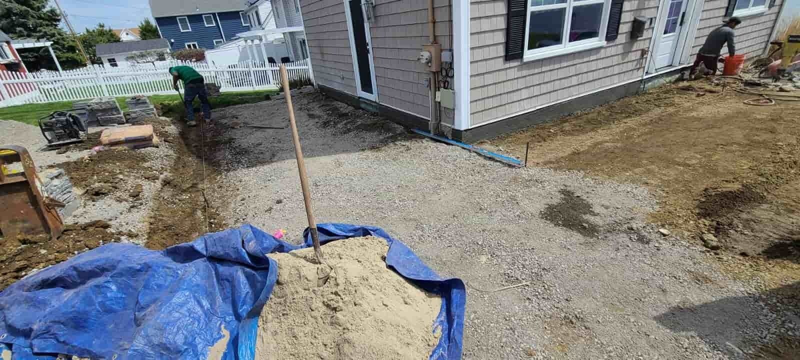 Backyard gravel work near a house, with blue tarp and construction materials.