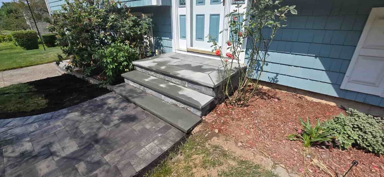 Front entry with concrete steps, blue siding, white doors, and landscaped mulch beds
