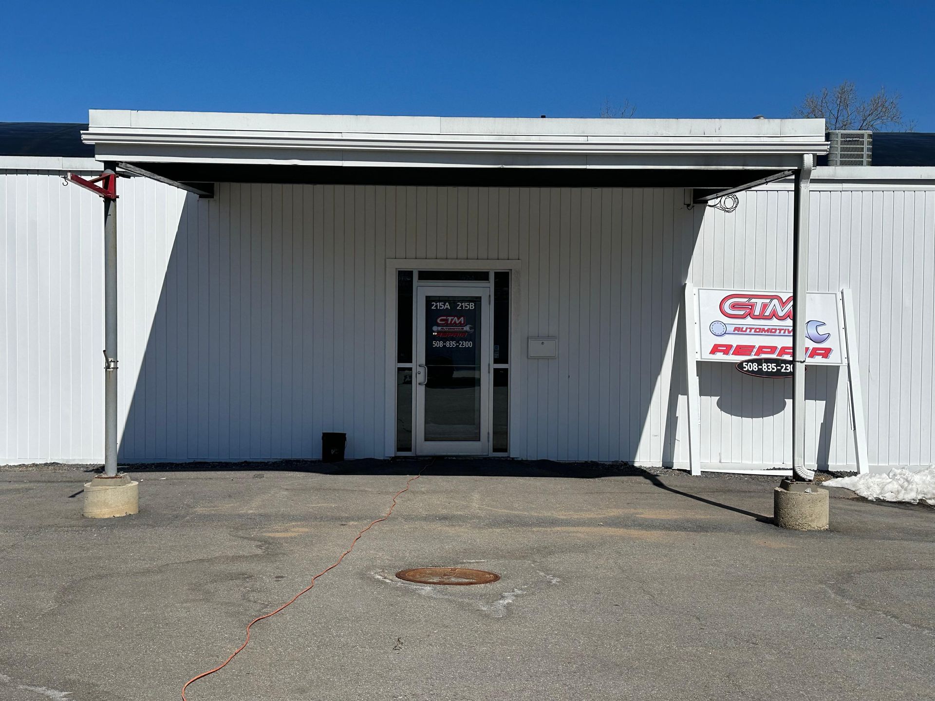 Exterior of a white metal industrial building with a covered entryway, central glass door, and a sign to the right.