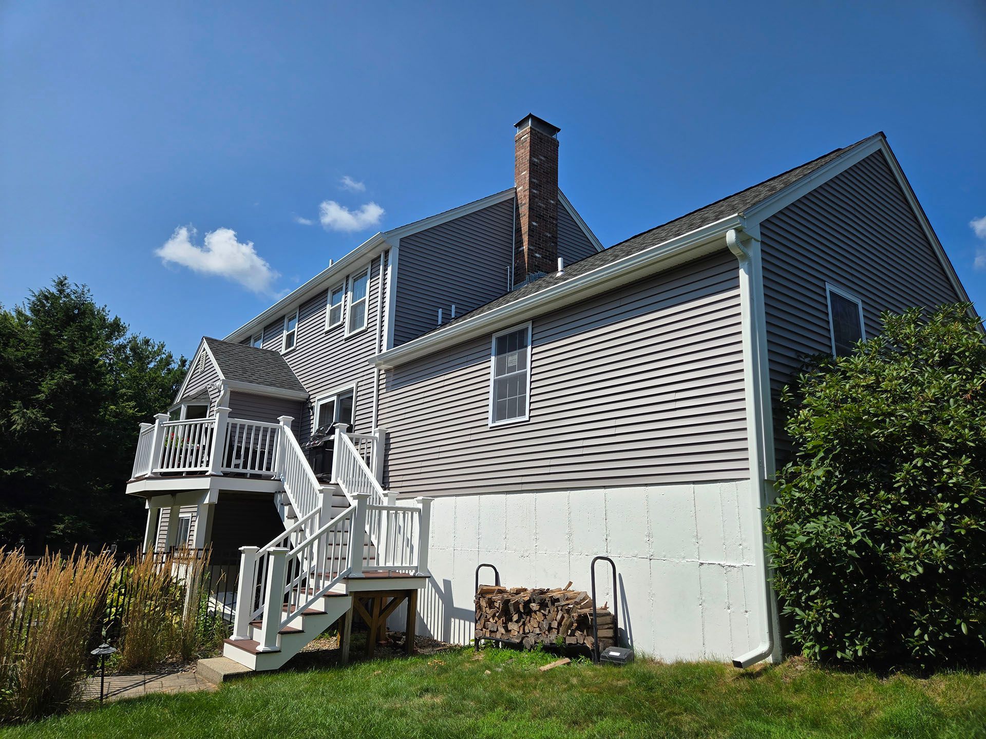 White-sided house with porch and staircase under a blue sky, surrounded by greenery