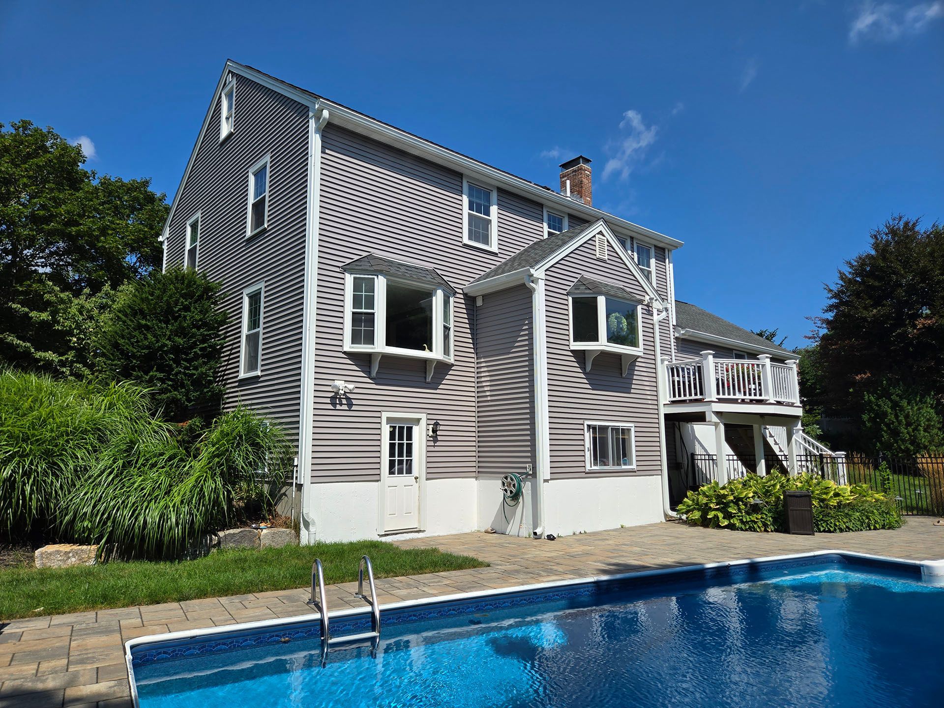 Gray house with white trim beside a blue swimming pool under a clear sky