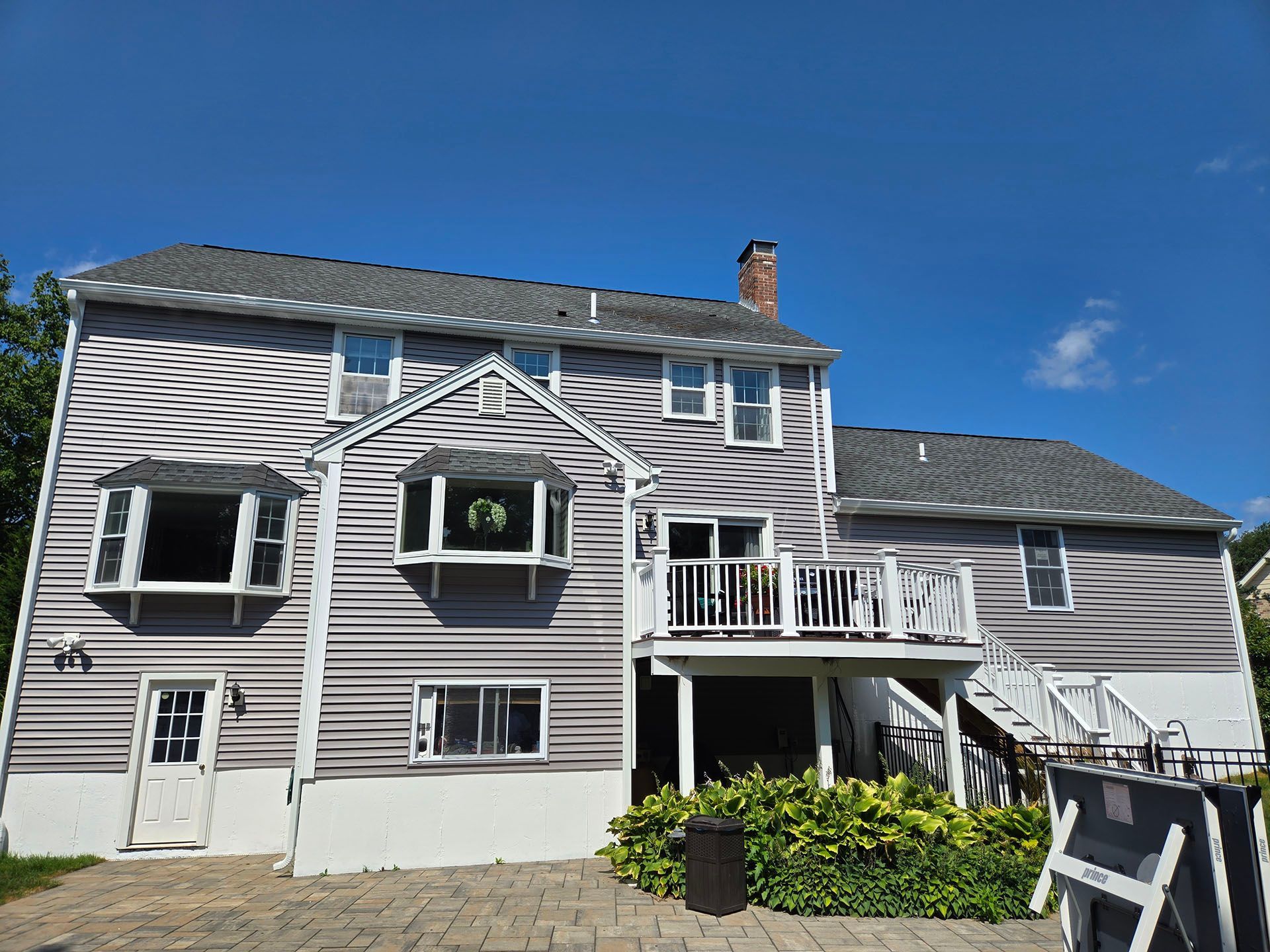 White two-story house with gray roof and deck, front view under a clear blue sky