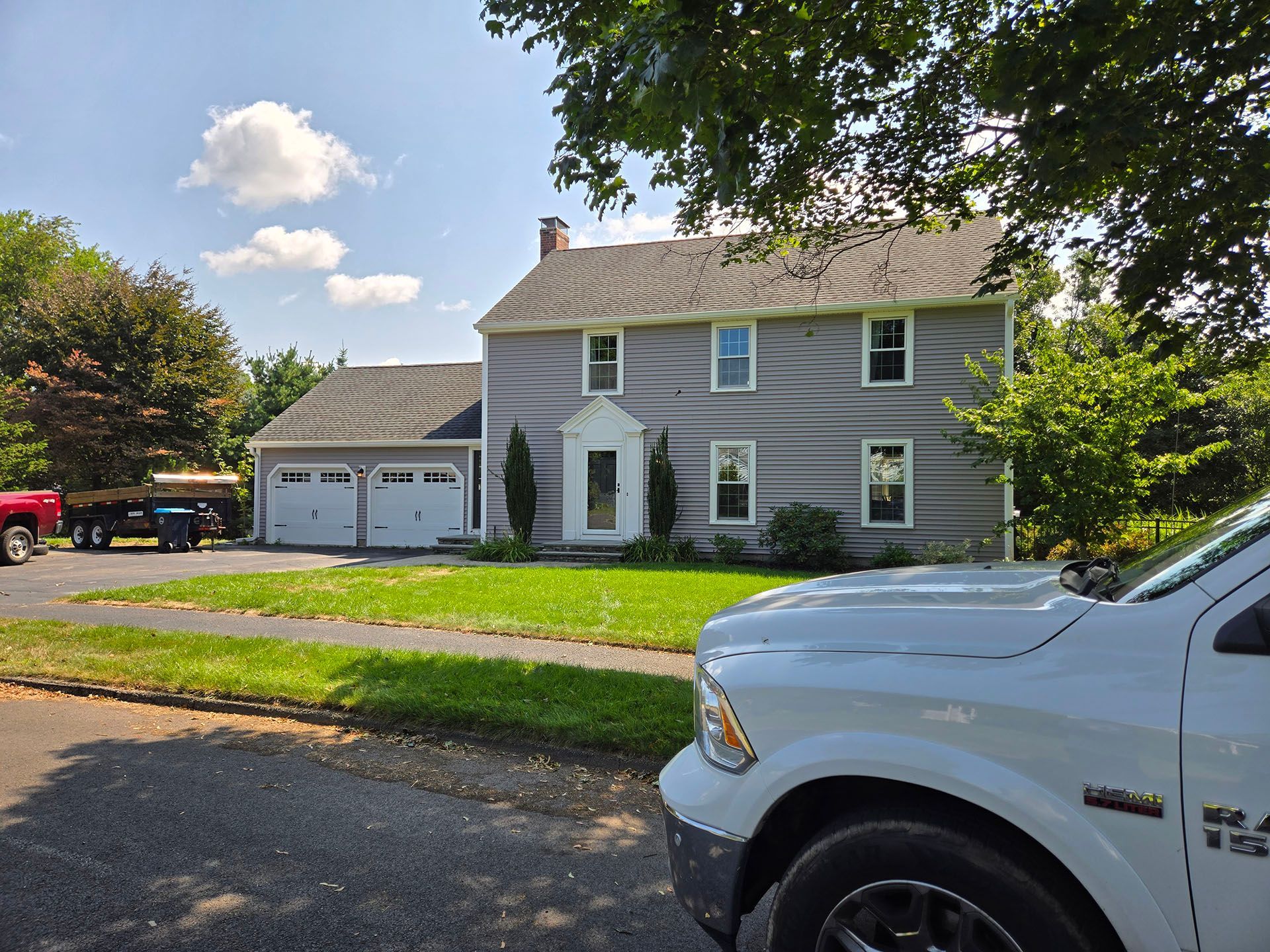 Suburban two-story house with garage, front lawn, and a white pickup truck in the foreground