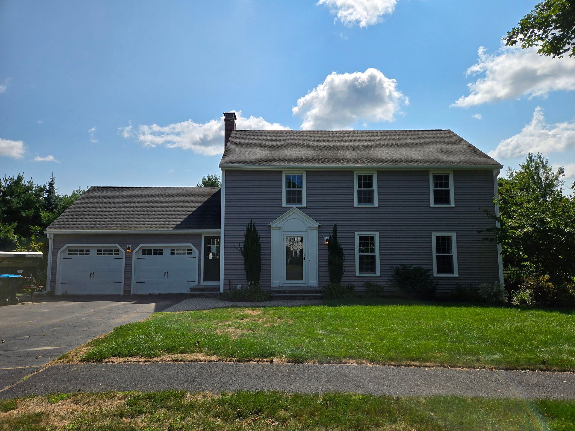 Two-story gray house with attached two-car garage, green lawn, and blue sky with clouds