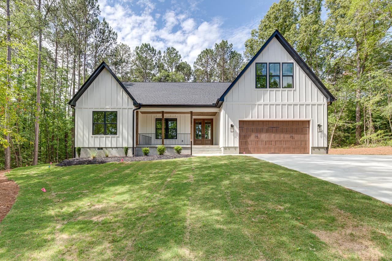 A white house with a black roof is sitting on top of a lush green field.