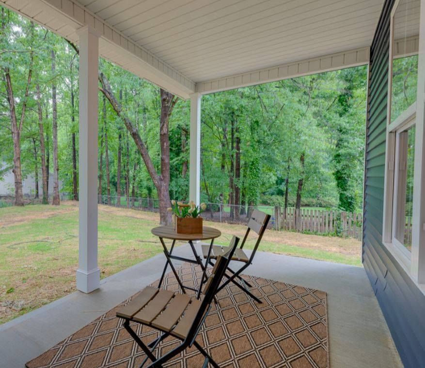 There is a table and chairs on the porch of a house.