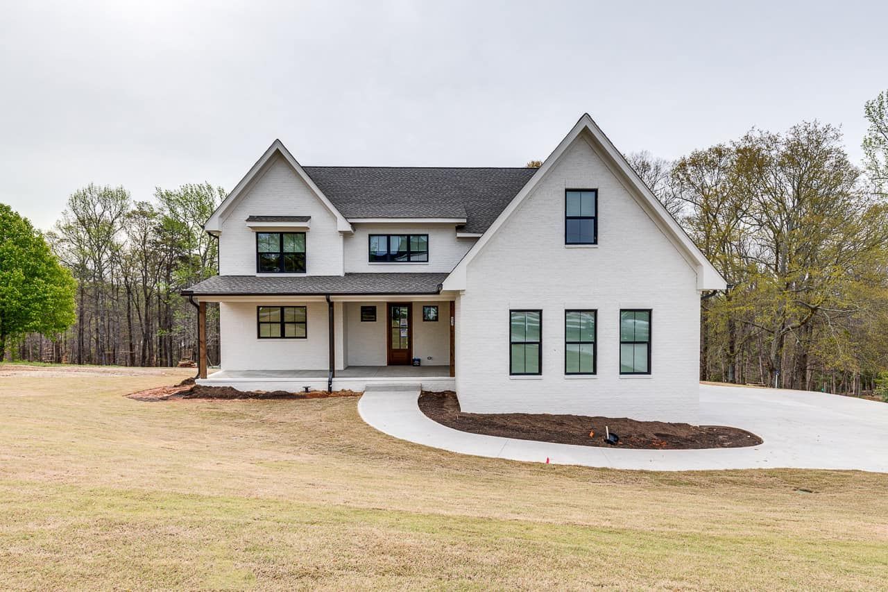 A white house with a gray roof is sitting in the middle of a grassy field.