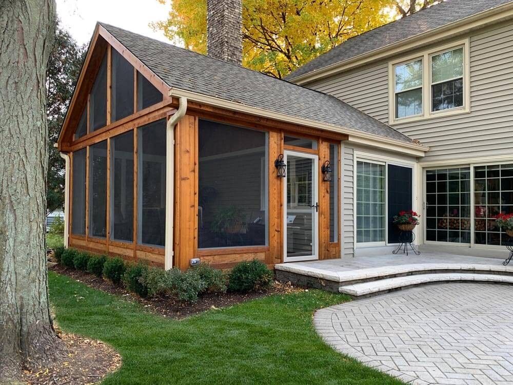 Screened porch addition with wooden frame and dark screens, attached to a house with sliding glass doors.