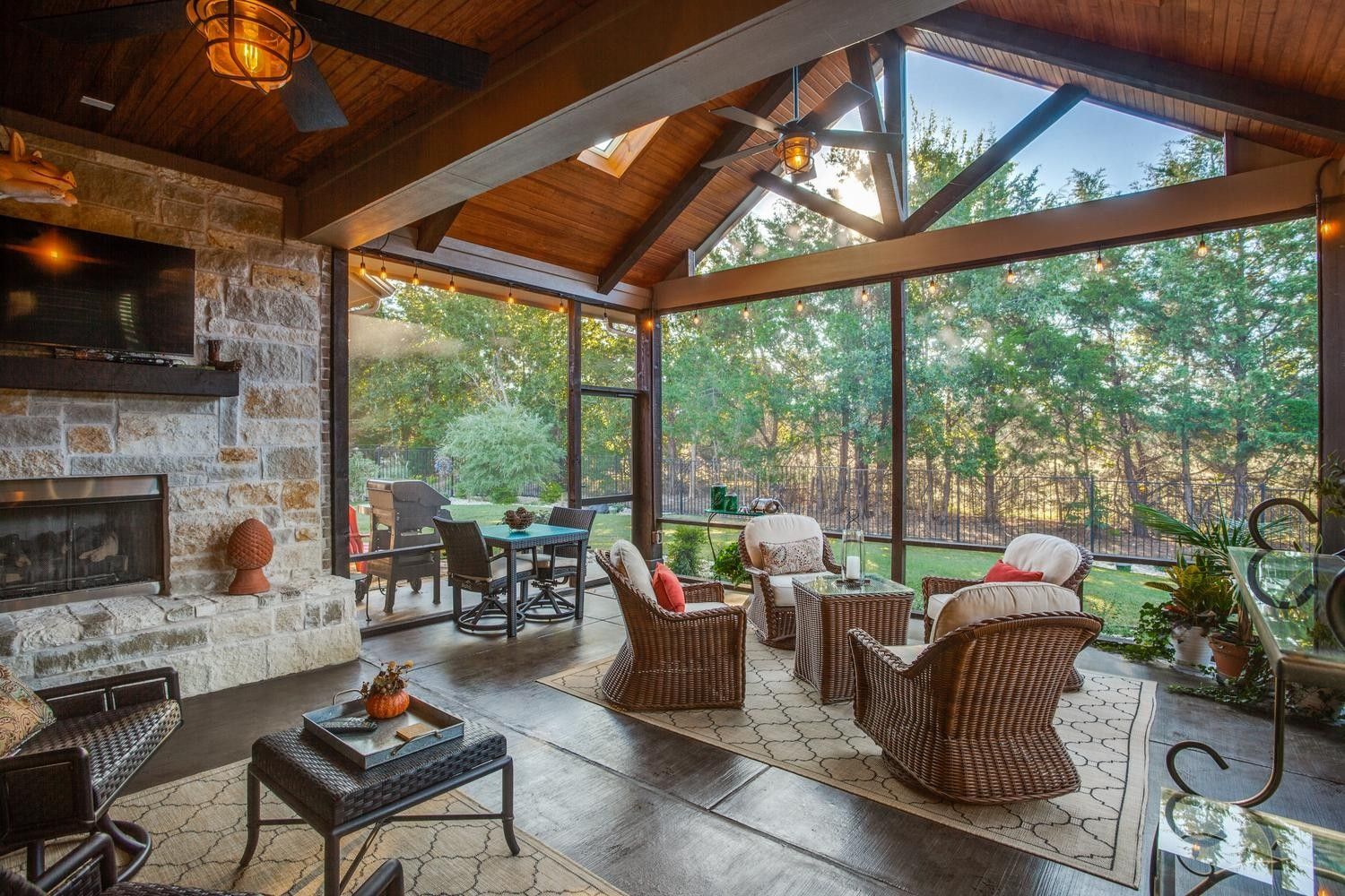 Screened-in porch with fireplace, seating area, and dining space, overlooking a wooded area.