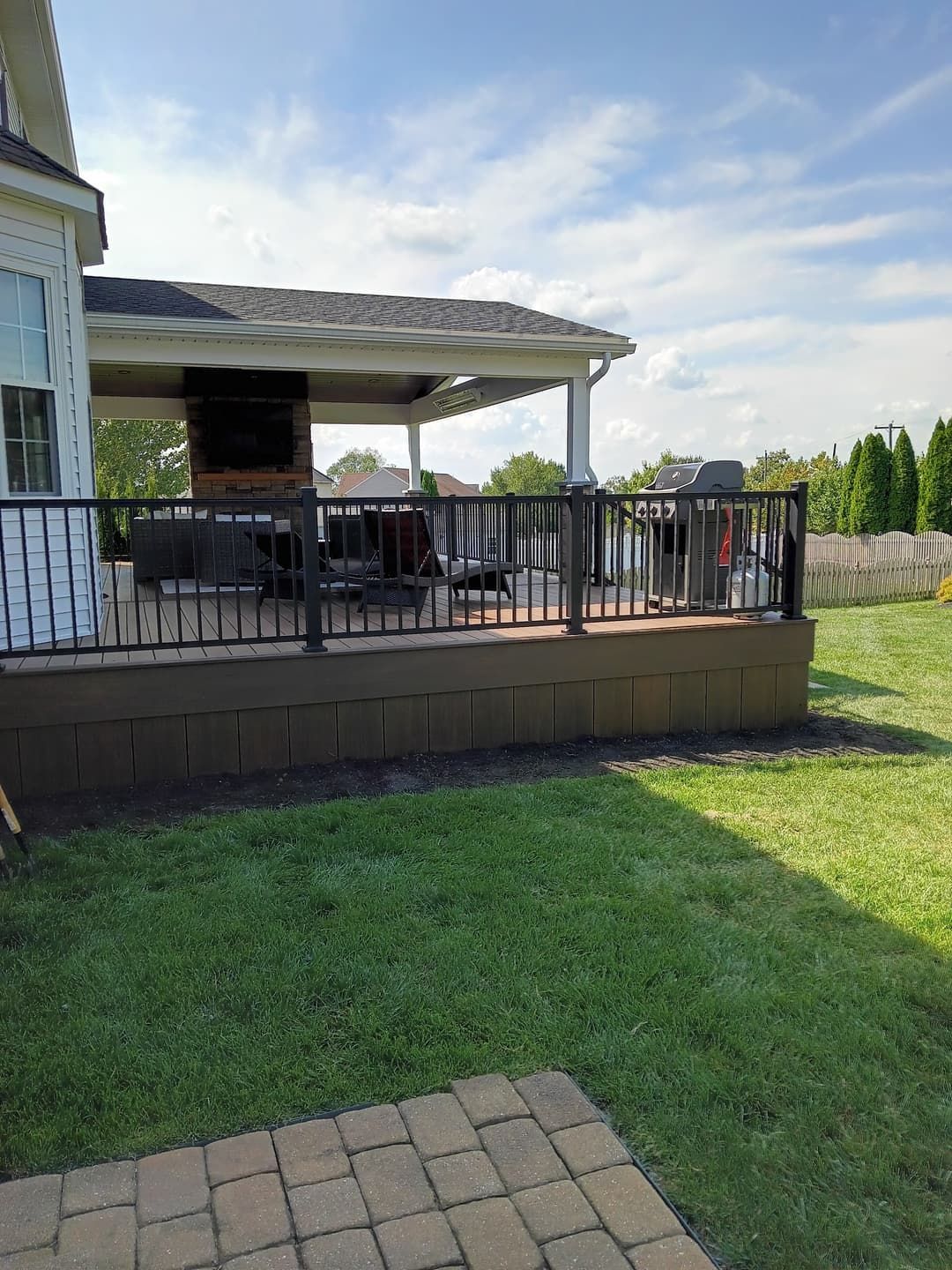Deck with black railing, overlooking a lawn. Covered patio area with outdoor furniture visible.