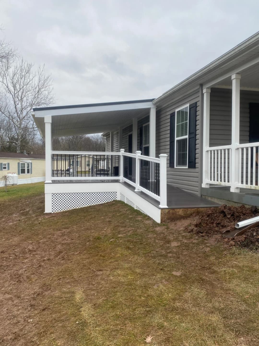 Covered porch with white and black railings, next to a gray house, on a grassy hill.