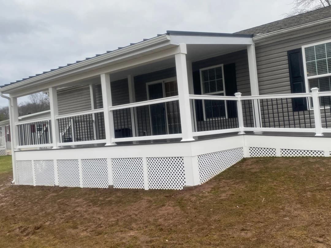 White porch on a gray house with a black railing. The porch has lattice skirting and a white roof.