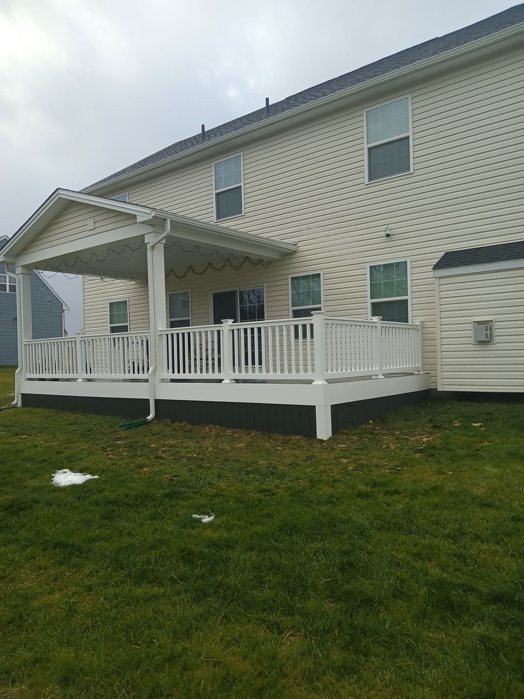 White deck with covered patio attached to a beige house, overlooking a grassy yard.