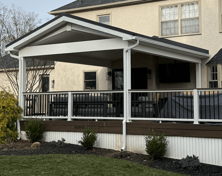Covered deck with black railing, overlooking a yard, attached to a light beige house.
