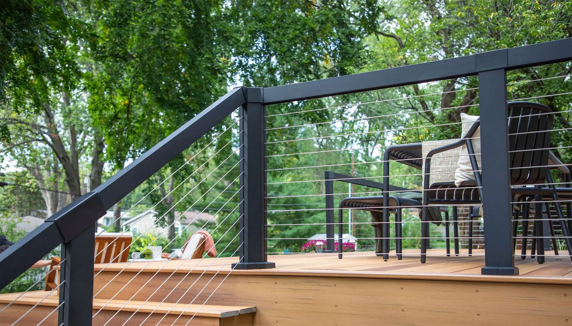 Deck with black railing, cable infill, and outdoor seating. Trees in the background.
