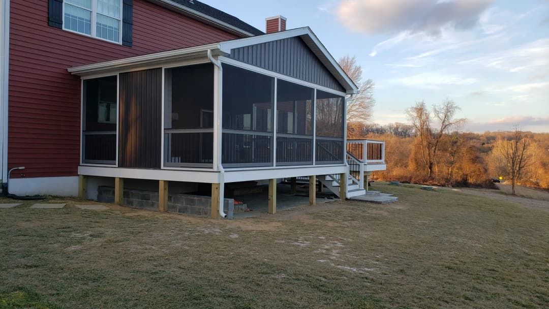 Screened-in porch attached to a red house, with white trim and wooden supports, set in a grassy yard.