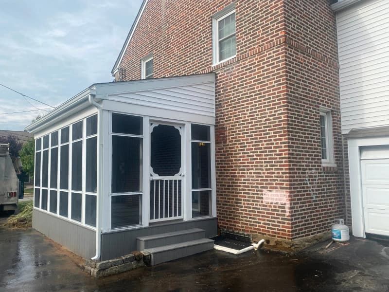 Screened-in porch attached to a brick house with steps. White trim, gray base, and a white garage door.