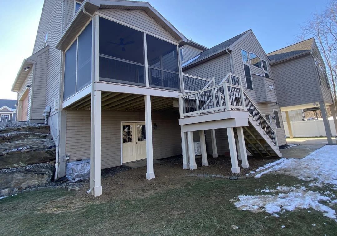 Back view of a two-story beige house with multiple decks, including a screened-in porch with a set of double doors.