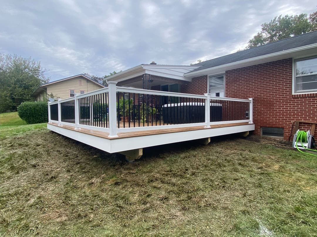 Deck with white railings and black spindles attached to a red brick house and a grassy yard.