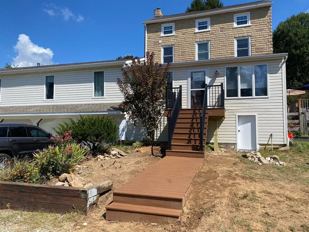 House with brown deck and stairs leading up from the yard, with a tan brick house in the background.