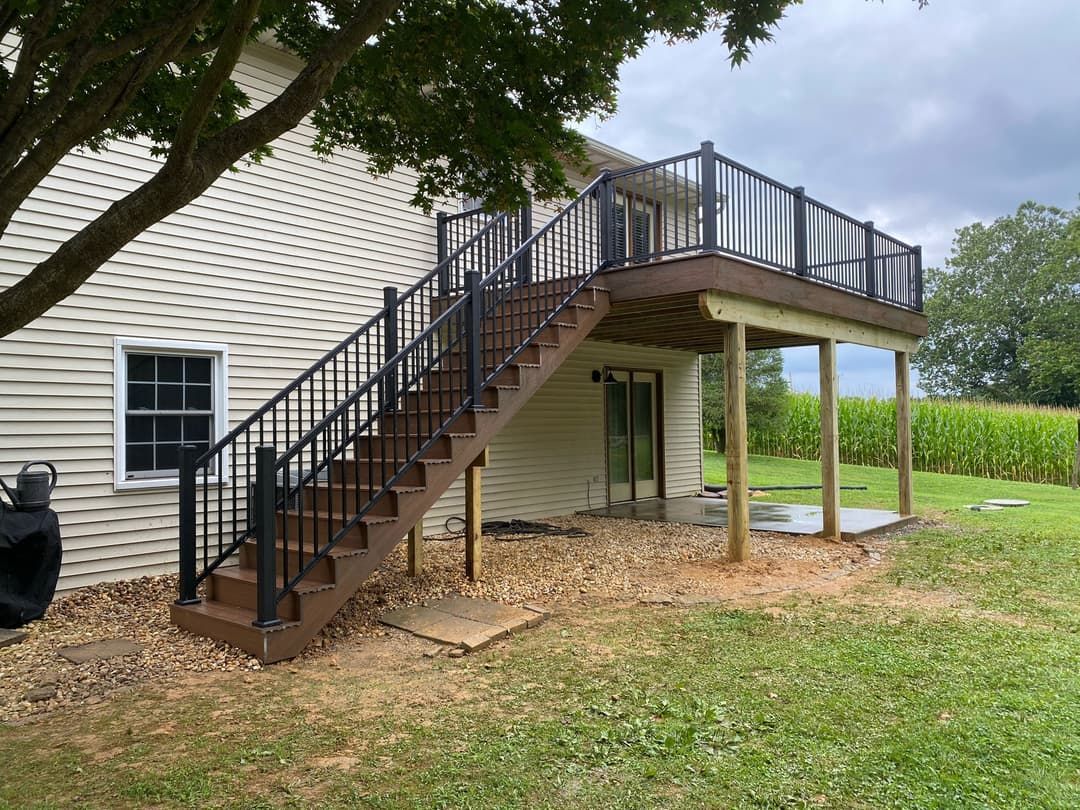 A two-story deck with stairs leading up to it, built onto a house with a cornfield in the background.