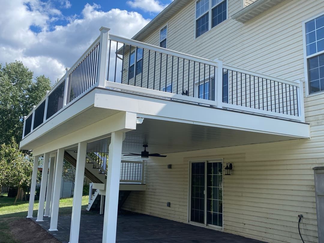 White deck with black railings and a covered patio beneath. Attached to a beige house with a sliding glass door.