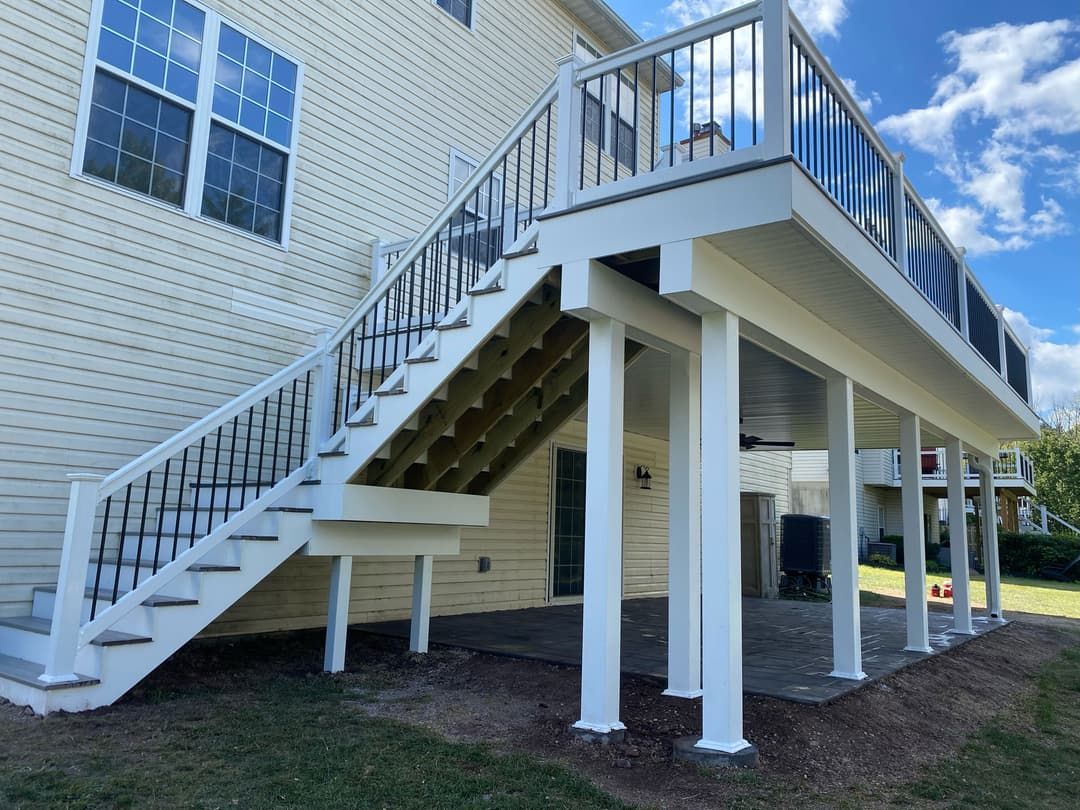 Elevated deck and stairs attached to a light yellow house with white supports and railing. Blue sky visible.