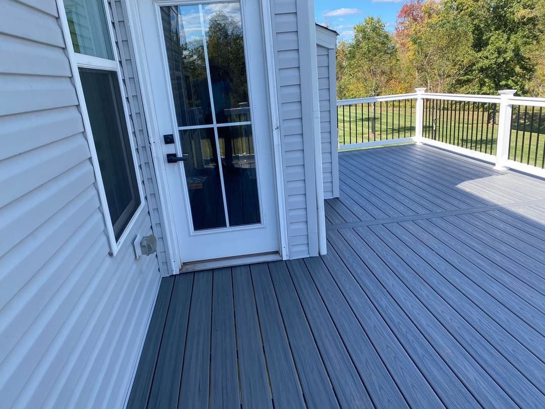 Gray composite deck with a white door and siding. Black railing and trees in the background.