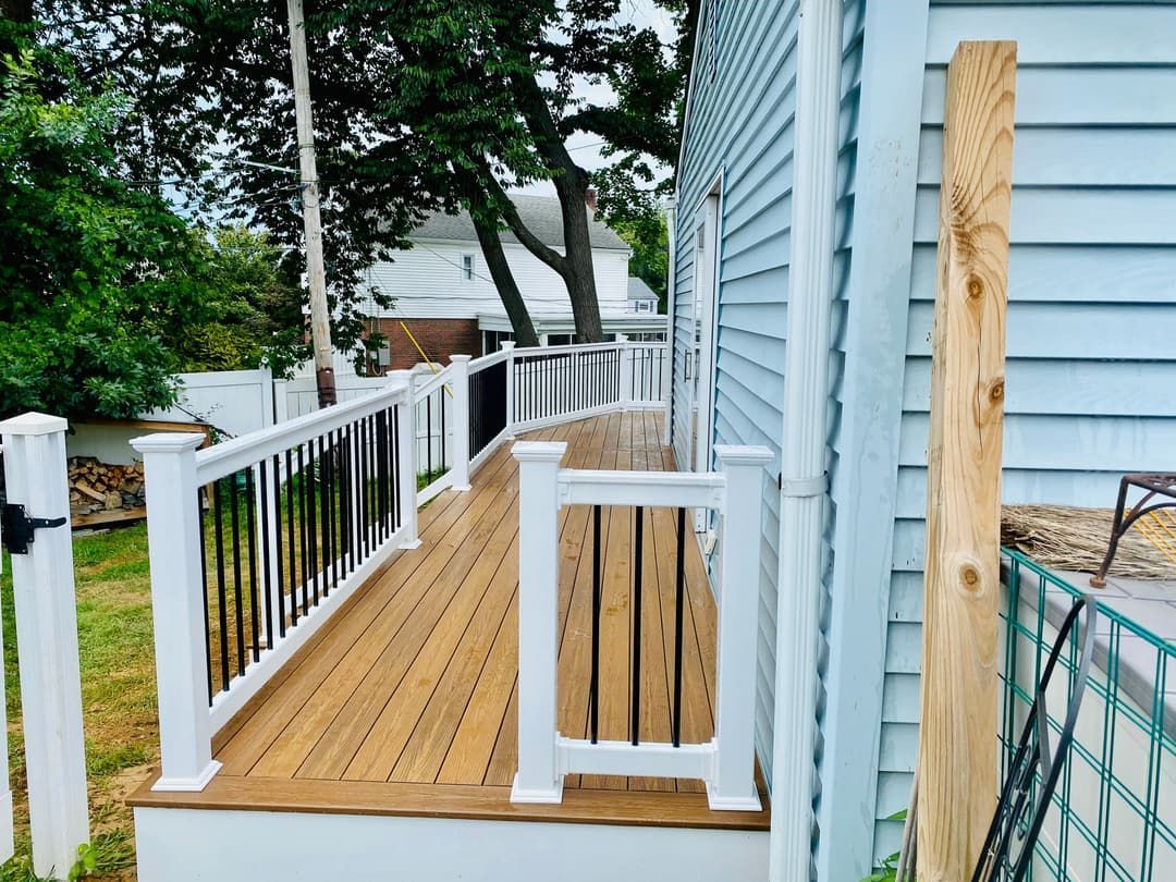 Wooden deck with white railings and black spindles next to a light blue house.