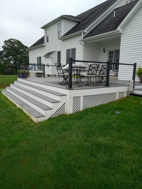 White house with composite deck and steps, black railing, lattice skirting, green lawn.