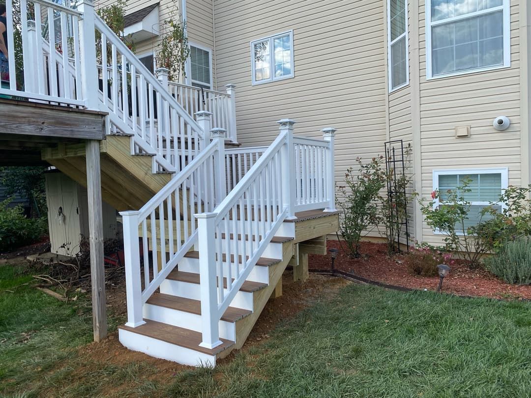 White railing and stairs leading down from a deck to a grassy yard, next to a beige house.