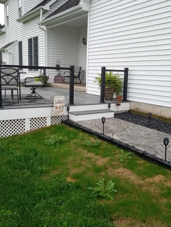 White house with a small deck and walkway, green grass, black edging, and solar lights.