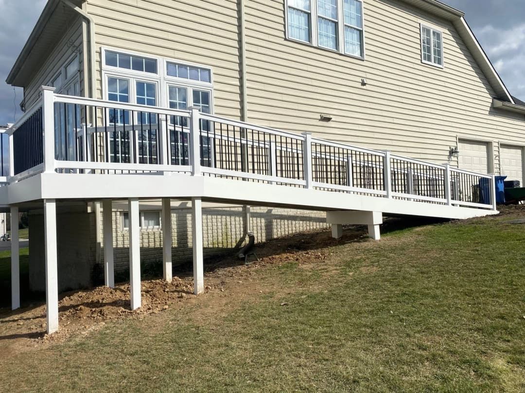 White elevated deck with ramp on grassy hillside, attached to a light-colored house.