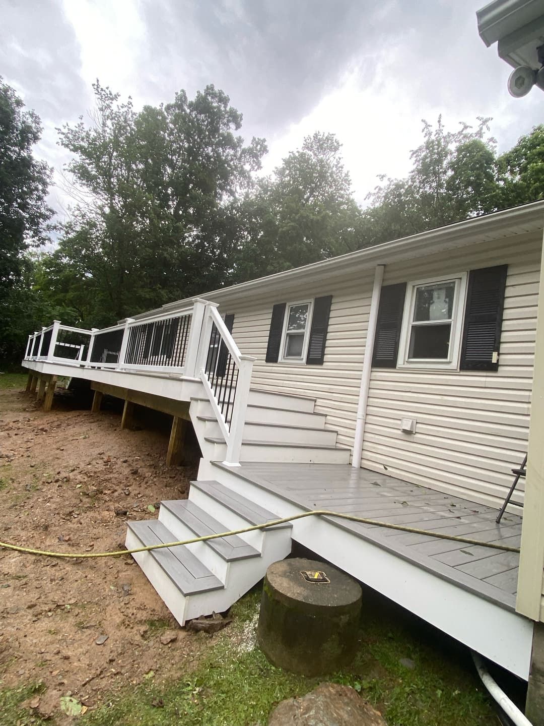 Exterior of a house with a newly constructed deck and stairs.  Gray deck with white railing, steps, and siding.