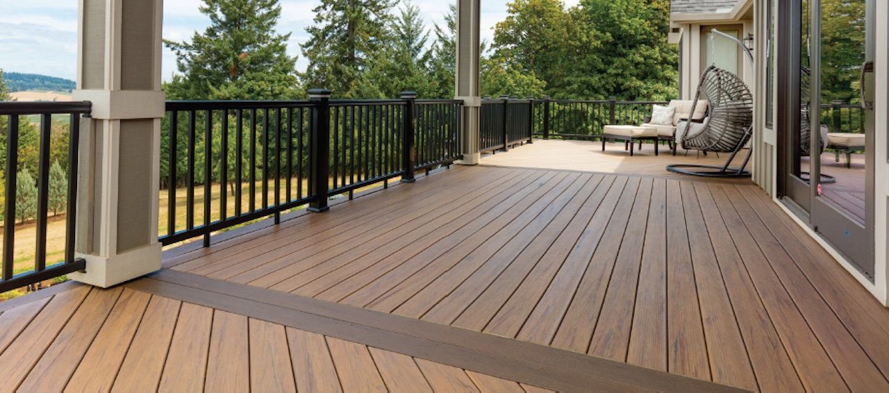 A wooden deck with a black railing overlooks a treeline.