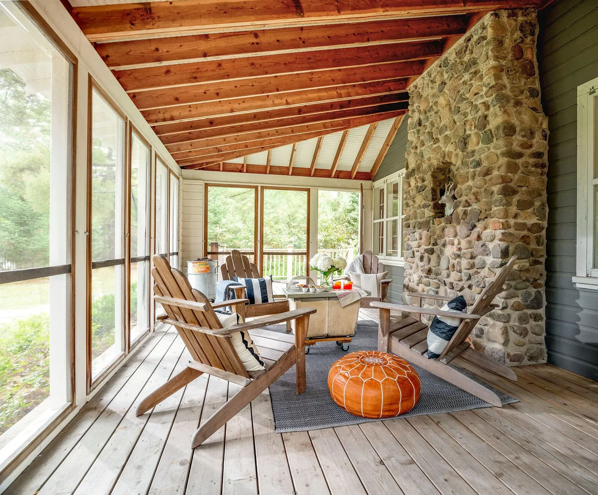 Screened-in porch with wood furniture, stone fireplace, and orange ottoman.