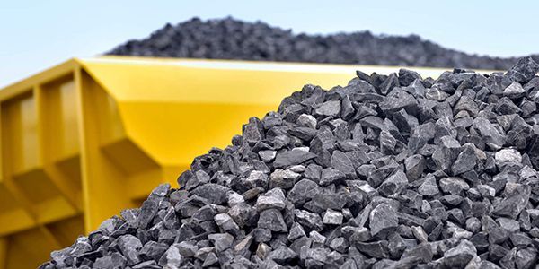 A pile of coal is sitting next to a yellow dumpster.