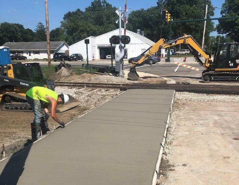A man is working on a concrete walkway next to a train track.