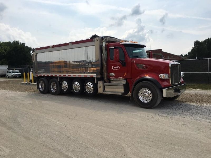 A red dump truck is parked on a dirt road