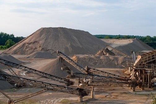 A large pile of dirt is sitting on top of a conveyor belt in a quarry.