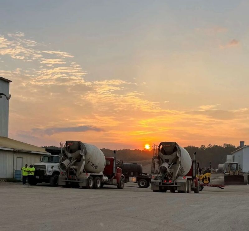 Two cement trucks are parked in a parking lot at sunset.
