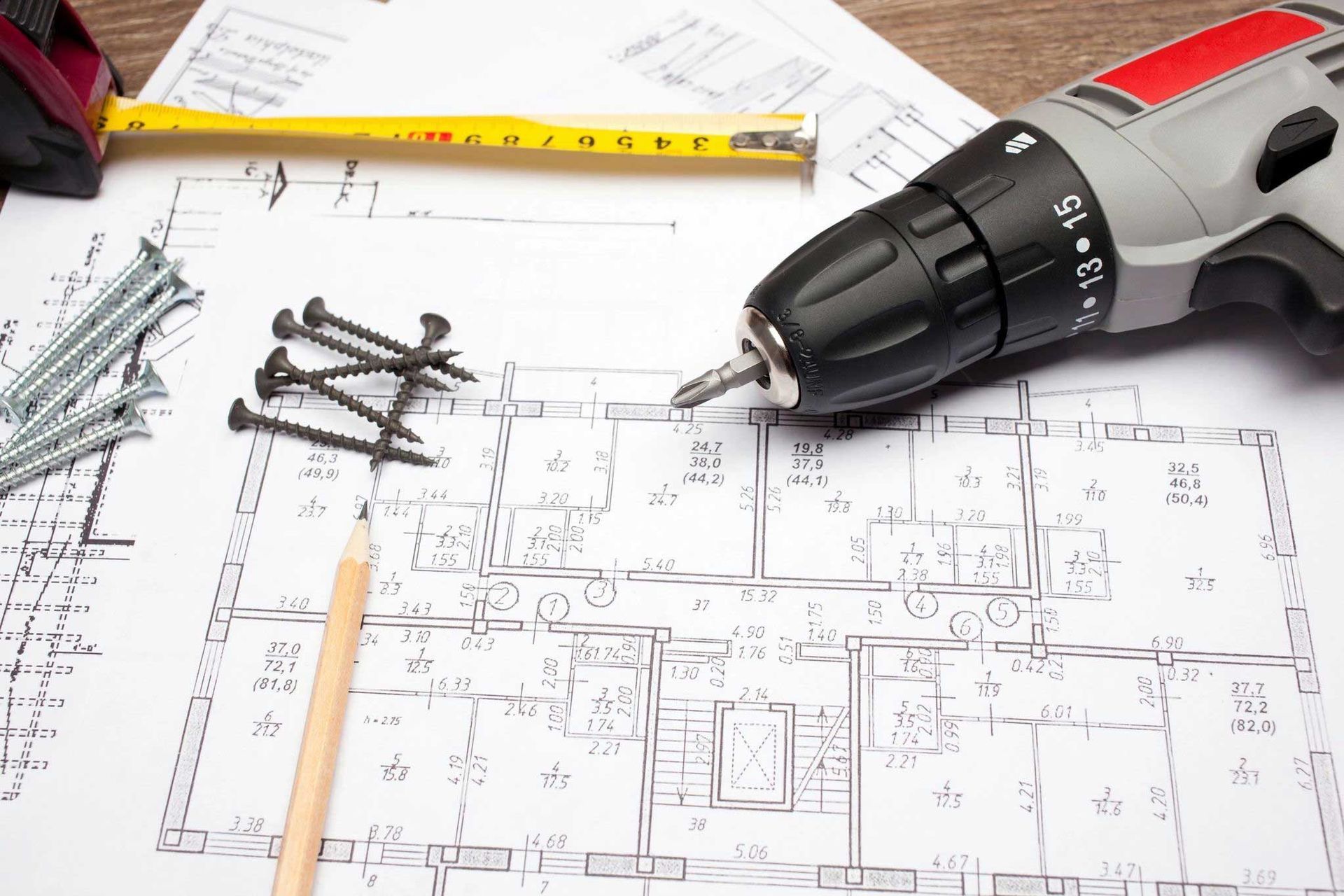 Drill, pencil, ruler, nails, and house blueprints on a worktable
