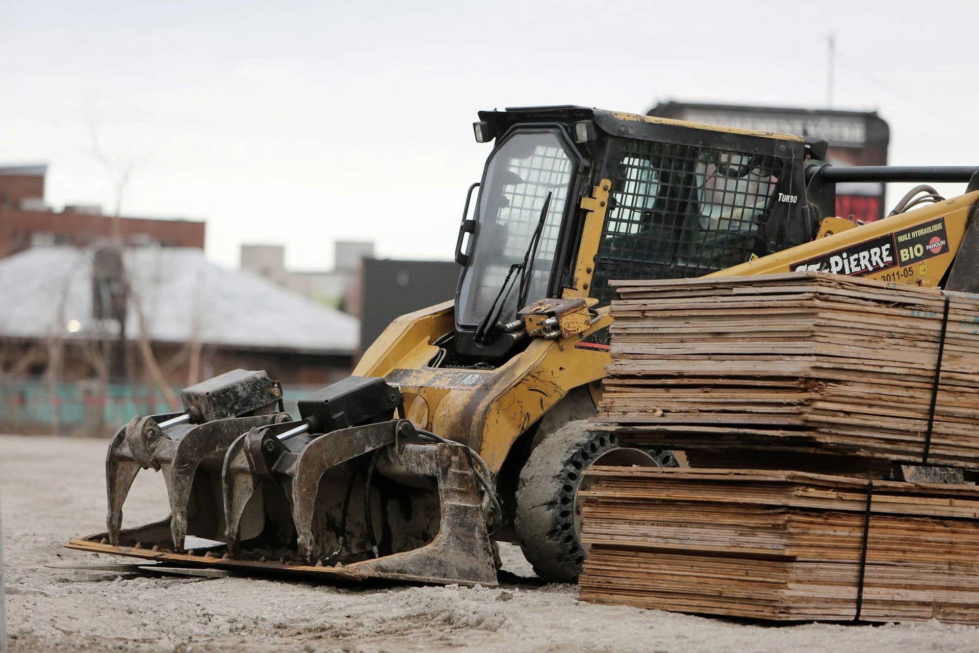Yellow bulldozer pushing stacked lumber on a muddy construction site