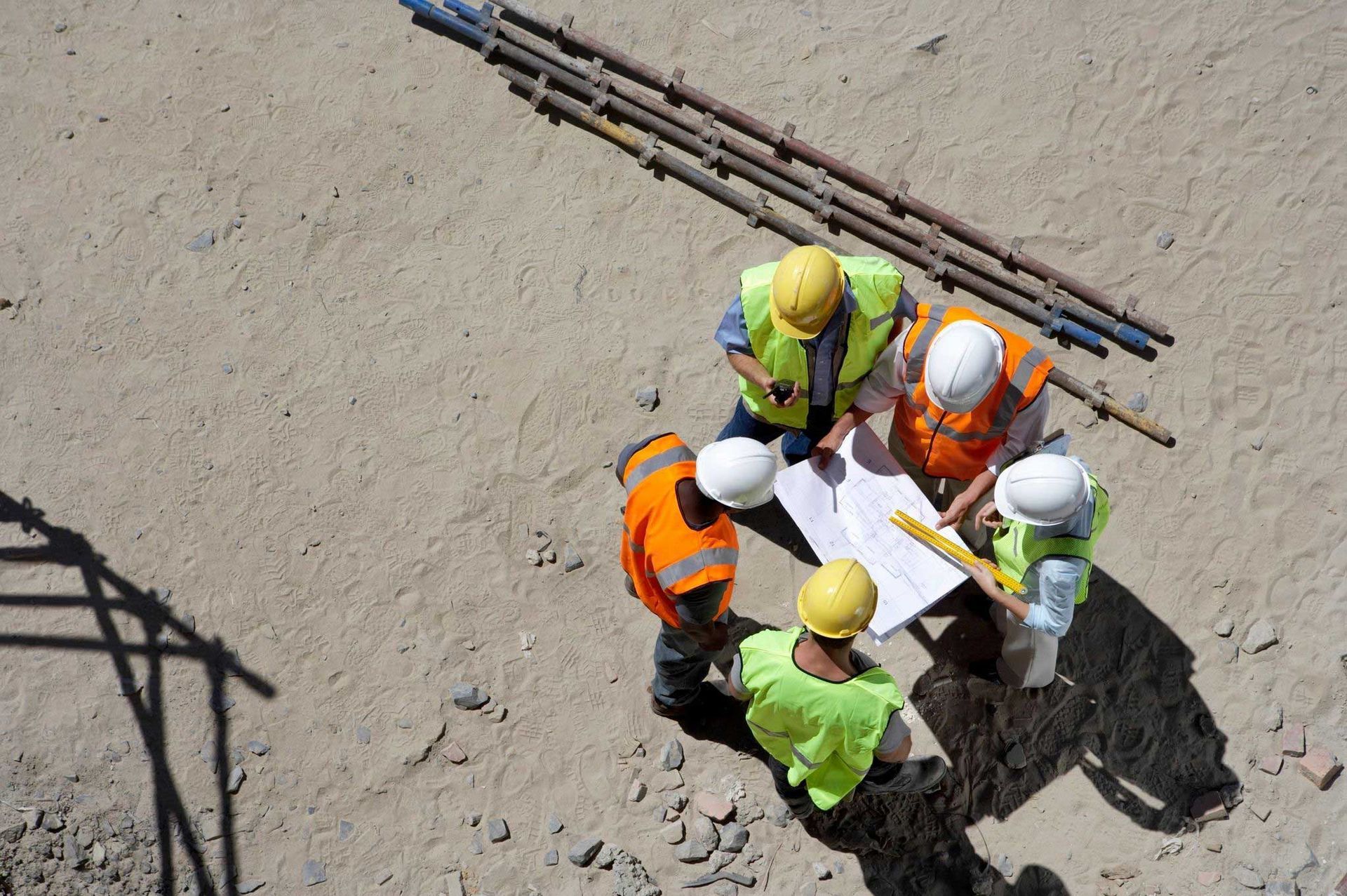 Construction workers in hard hats huddle over plans at a building site.