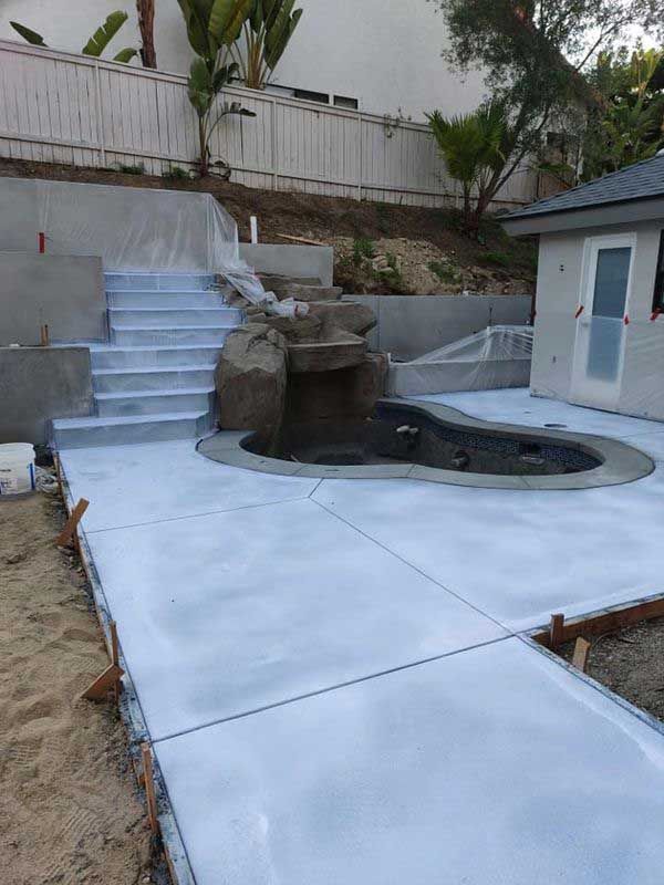 Backyard with a newly plastered white patio, steps, and a small curved pool or spa.